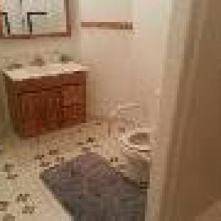 A bathroom with a double sink, toilet, and tiled floor.