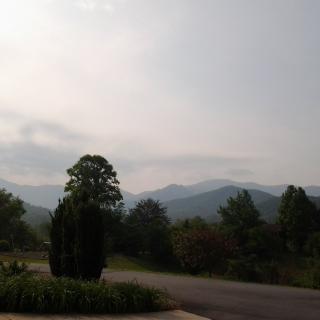 A scenic view of distant mountains under a clear sky, framed by trees and a winding road.