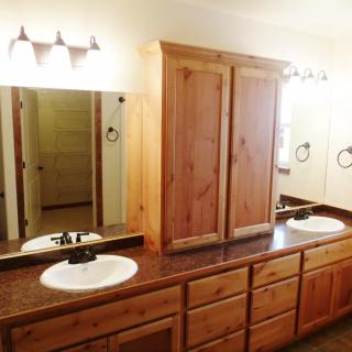 A bathroom featuring a double sink with wood cabinetry and mirrored lighting.