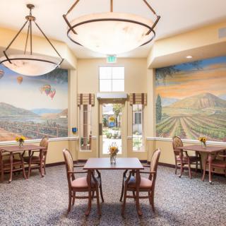 A well-lit dining area with murals on the walls, featuring tables and chairs arranged under large chandeliers.