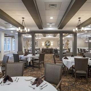 An elegant dining room with neatly arranged tables and chairs, featuring subdued lighting and decorative elements.