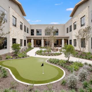 A landscaped courtyard featuring a small putting green surrounded by a two-story building.