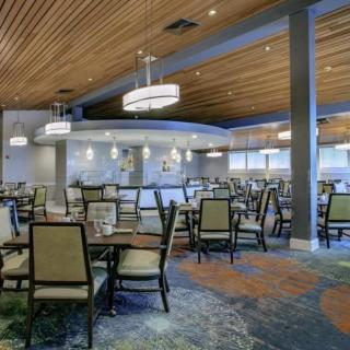 A modern restaurant interior with neatly arranged tables and chairs, illuminated by stylish ceiling lights.