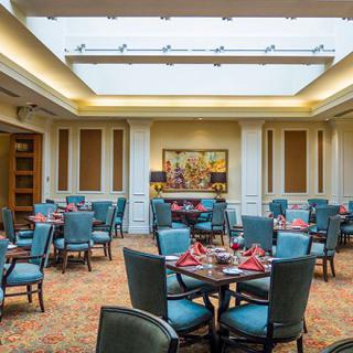 A well-lit dining room with multiple tables and chairs arranged under a large skylight.