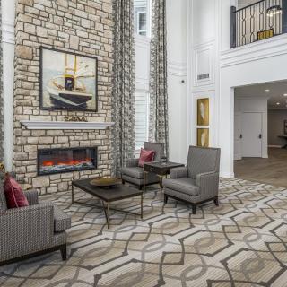 A modern living room featuring a stone fireplace, stylish armchairs, and a high ceiling.
