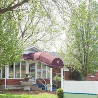 A quaint brick house with a maroon awning, surrounded by lush green trees, illustrating a serene spring setting.