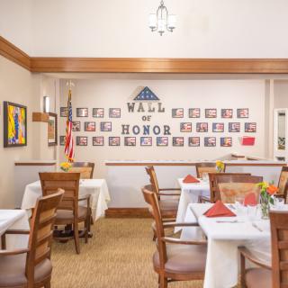 A neatly arranged dining room with a Wall of Honor displaying photos, decorated in a patriotic theme.