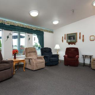 A cozy living room with several comfortable armchairs arranged around a table, decorated with lamps and artwork on the walls.