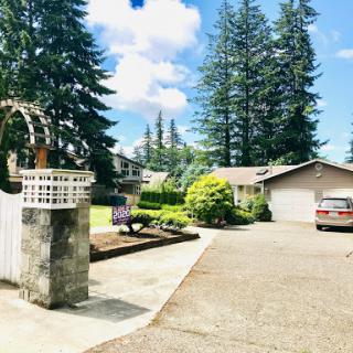 A serene residential scene featuring a driveway leading to a cozy house, surrounded by tall trees and well-maintained landscaping.