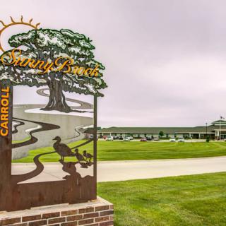 A scenic view of a park entrance with a decorative sign in the foreground and lush greenery surrounding the area.