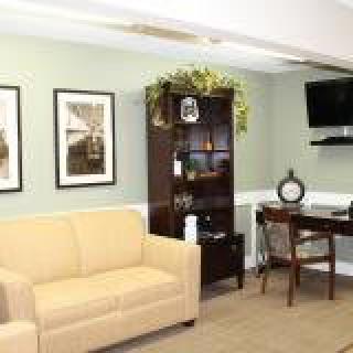 A cozy living room with a beige sofa, dark wood desk and shelf, wall-mounted TV, and decorative accents.