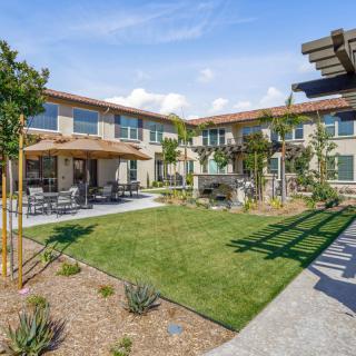 A sunny courtyard featuring a landscaped garden and outdoor seating area, surrounded by a residential building.