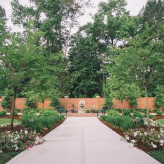 A serene garden pathway lined with lush trees and vibrant flower beds, inviting visitors into a peaceful outdoor space.