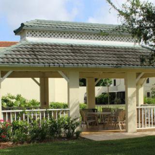 A charming gazebo with a tiled roof and outdoor furniture set in a manicured garden.
