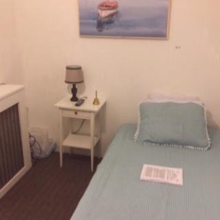 A cozy and minimalistic bedroom featuring a single bed, a nightstand with a lamp, and a calming piece of artwork.