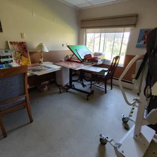 A bright and spacious workspace featuring a desk, chair, and art supplies near a window.