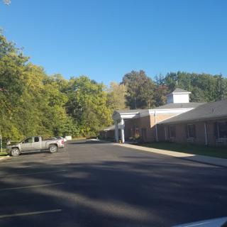 A serene view of a building along a tree-lined road under a clear blue sky.