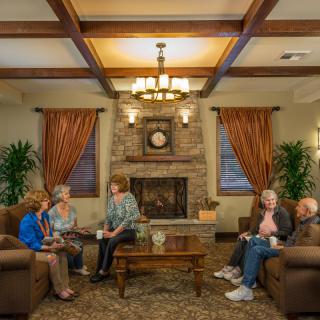 A cozy living room with seniors engaging in conversation around a coffee table by the fireplace.