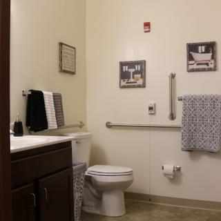 A clean and neatly organized bathroom featuring a toilet, sink with towels, and wall decor.