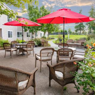A cozy patio with rattan furniture and red umbrellas, surrounded by a lush garden.