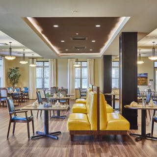 A modern restaurant interior with yellow booth seating, tables, and chairs on a wooden floor.