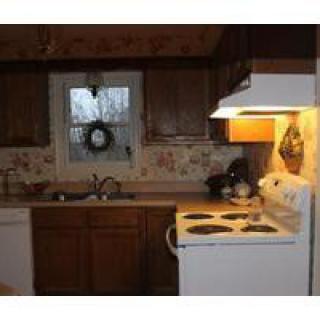 A cozy kitchen with wooden cabinets, a stove, and a window above the sink.
