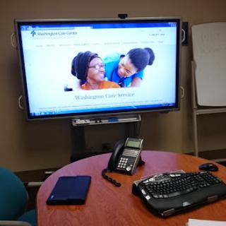 An office meeting room featuring a large screen display, a phone, and a keyboard on the table.