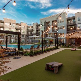 Modern apartment complex with a courtyard featuring a swimming pool and ambient string lighting.