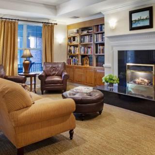 A cozy living room with a fireplace, armchairs, and a well-stocked bookshelf.