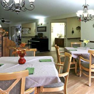 A cozy dining room setup with tables covered in tablecloths, surrounded by wooden chairs and decorated with chandeliers.