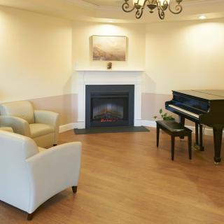 A cozy living room featuring a grand piano and a warm fireplace, complemented by comfortable seating.