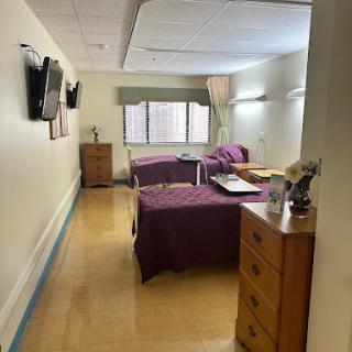 A spacious patient room in a hospital, featuring two beds with purple bedding and a warm, inviting atmosphere.