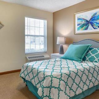 A cozy bedroom with teal and white bedding, a bedside lamp, and butterfly artwork on the wall.