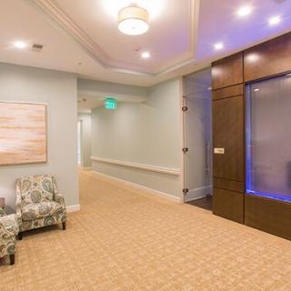 A well-lit hallway with an elevator, seating area, and artwork on the wall.