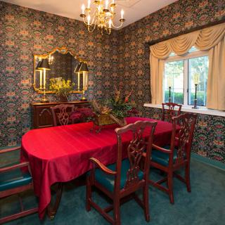A vintage-style dining room featuring a red tablecloth, ornate wallpaper, and a classic chandelier.