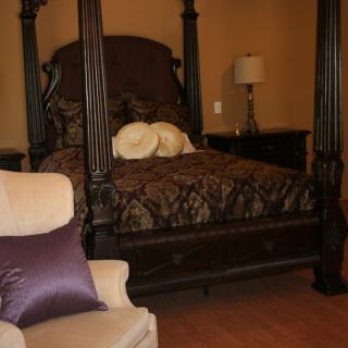 A cozy bedroom with a four-poster bed, an armchair, and a lamp on the nightstand.