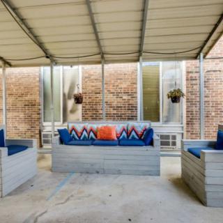 A cozy patio with cushioned seating under a canopy, decorated with colorful pillows and hanging plants.