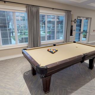 A pool table in a well-lit game room with large windows and curtains.