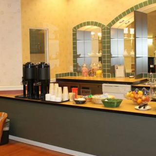 A kitchen area with a coffee station and breakfast bar, featuring various beverages and fresh fruit on the counter.
