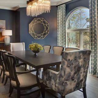 A modern dining room with blue walls, featuring elegant furniture, a chandelier, and a decorative mirror.
