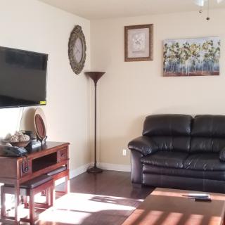 A cozy living room with a black sofa, wall-mounted television, and decorative art pieces.
