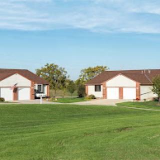 A peaceful suburban setting featuring two houses with a lush green lawn and blue sky.