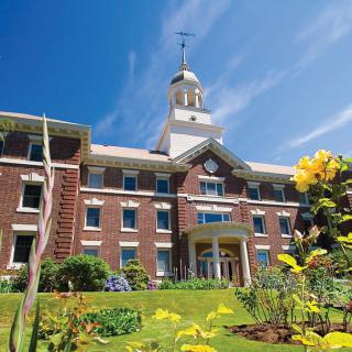A historic brick building with a clock tower surrounded by gardens on a sunny day.