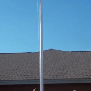 A tall flagpole stands in front of a building with a sloped roof against a clear blue sky.