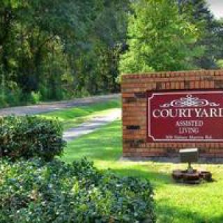 A brick sign for Courtyard Assisted Living beside a tree-lined road.