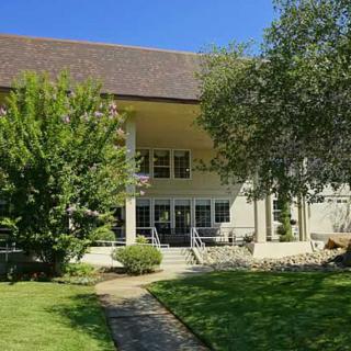 A sunny day view of a building surrounded by trees and a well-maintained lawn with a pathway leading to the entrance.