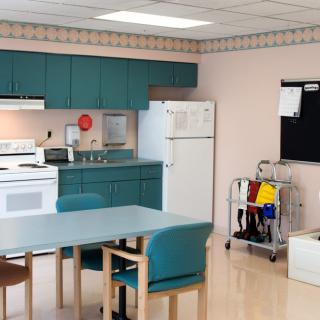 A kitchen with teal cabinets, dining table, and chairs alongside a refrigerator and stove.