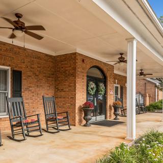 A cozy porch featuring rocking chairs and ceiling fans, attached to a brick building.