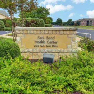 Stone sign for Park Bend Health Center surrounded by greenery.