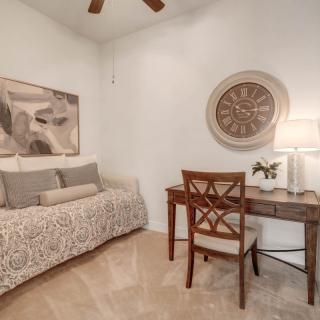 A cozy bedroom featuring a daybed, a desk with a lamp, and elegant wall art.